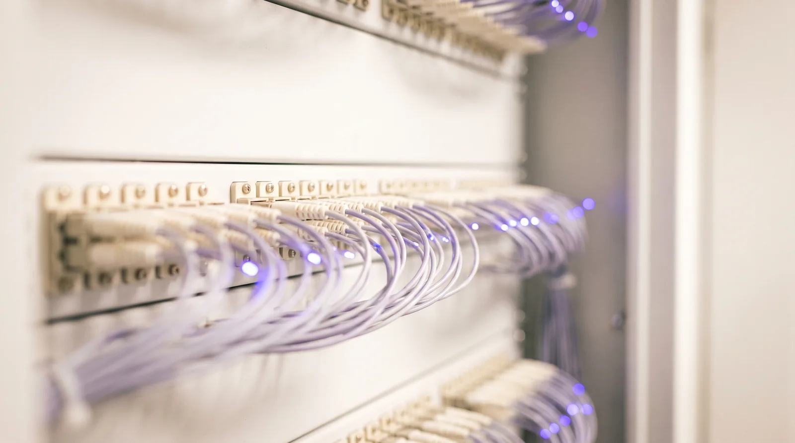 Panel de fibra óptica en un armario de comunicaciones, con los latiguillos peinados y los extremos de fibra iluminados.