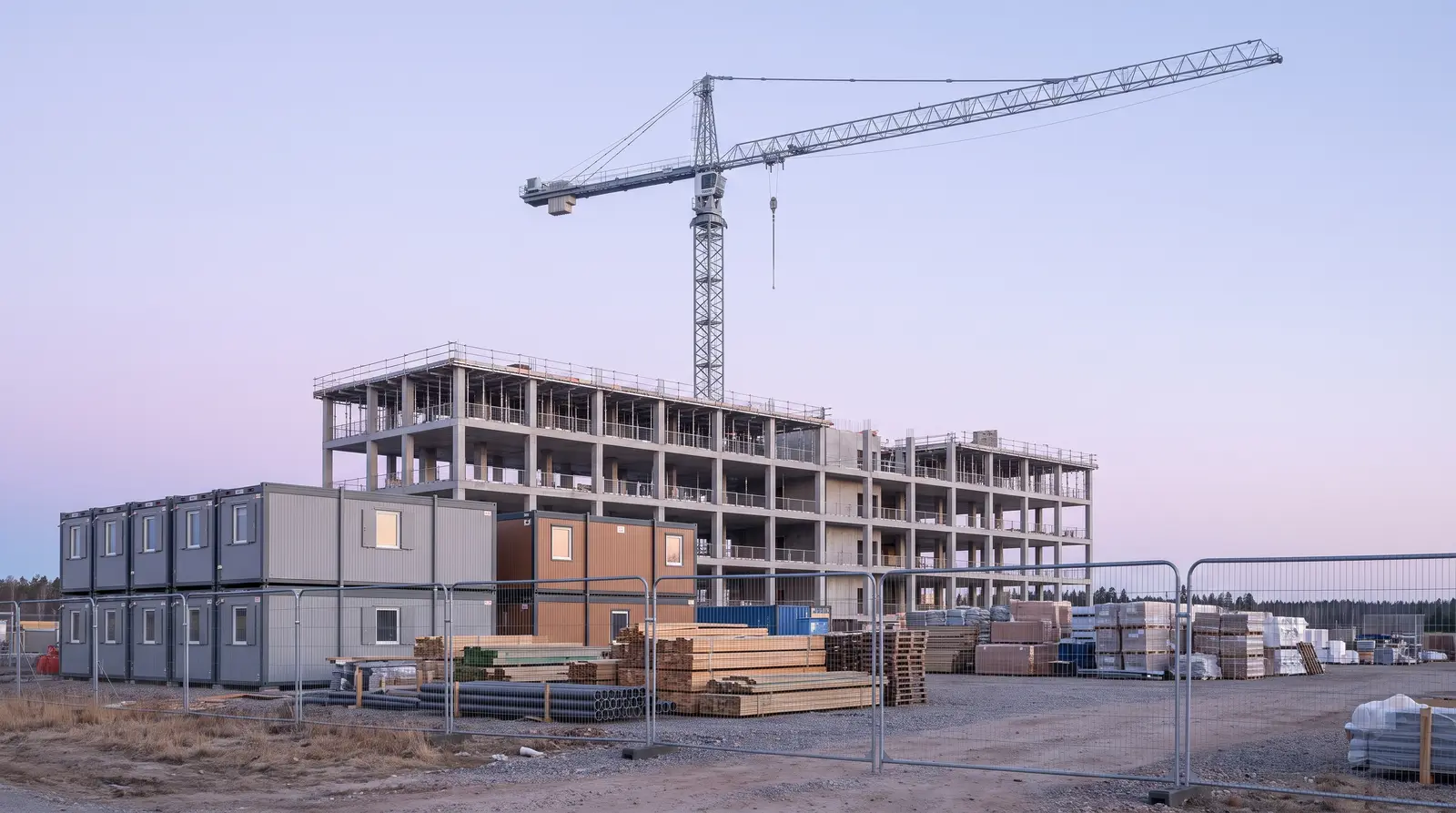 Obra de edificación con la estructura de hormigón en altura, grúa torre y casetas de obra tras el vallado