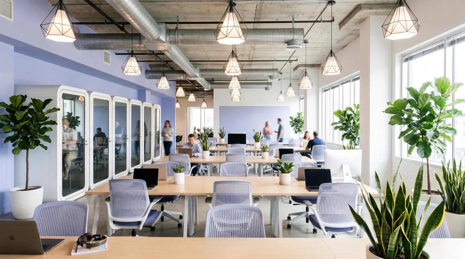 Espacio de coworking con puestos compartidos, cabinas acristaladas para llamadas y plantas, con gente trabajando al fondo