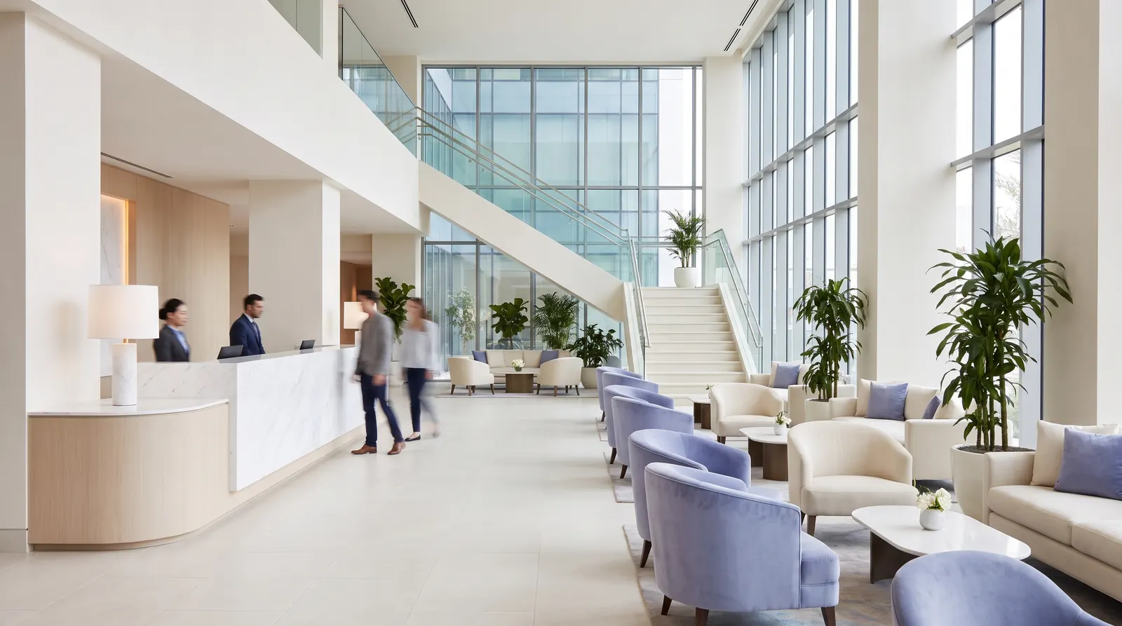 Vestíbulo de hotel con recepción, zona de estar y una escalera amplia, con luz natural entrando por el ventanal